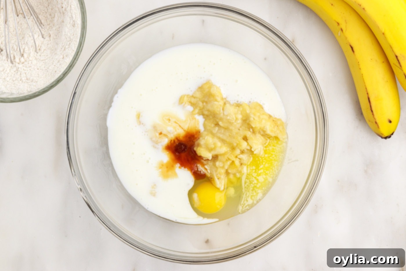 Wet ingredients for banana pancake batter including egg, melted butter, vanilla, buttermilk, and mashed banana in a large bowl.