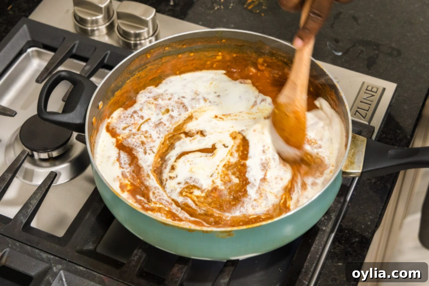 Stirring the creamy tomato sauce in a skillet, creating a rich orange color.
