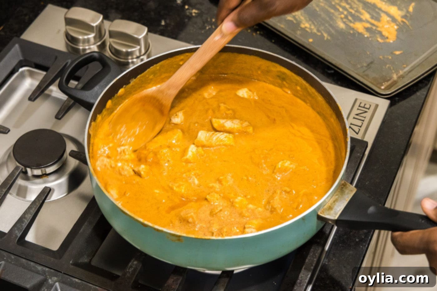 Stirring tender chicken pieces into the creamy Tikka Masala sauce in a skillet.