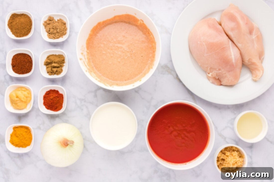 Assortment of fresh ingredients for Chicken Tikka Masala, including chicken, yogurt, spices, tomatoes, and cream.