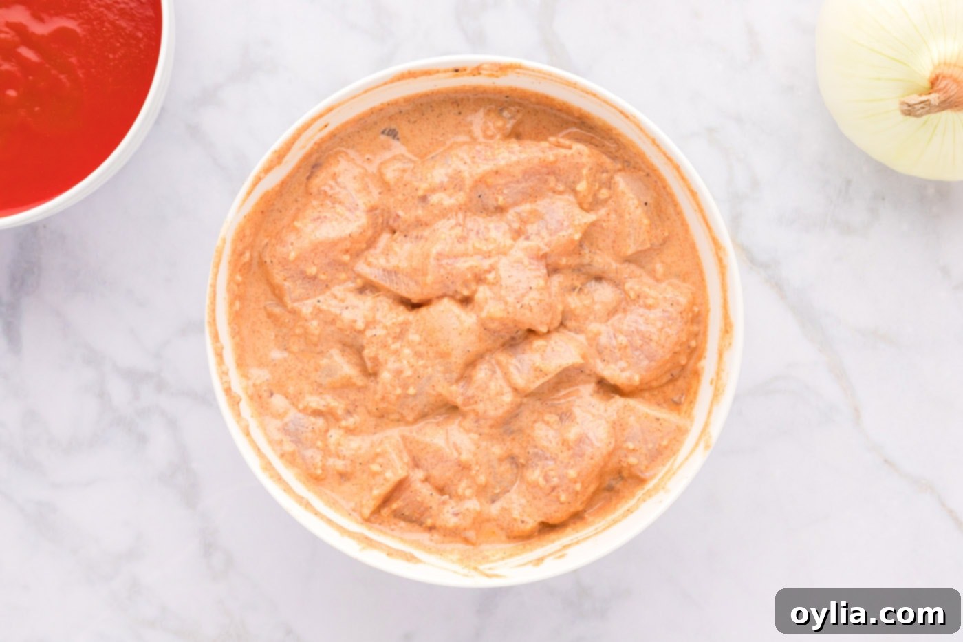 Cubed chicken marinating in a large bowl with yogurt and spices.