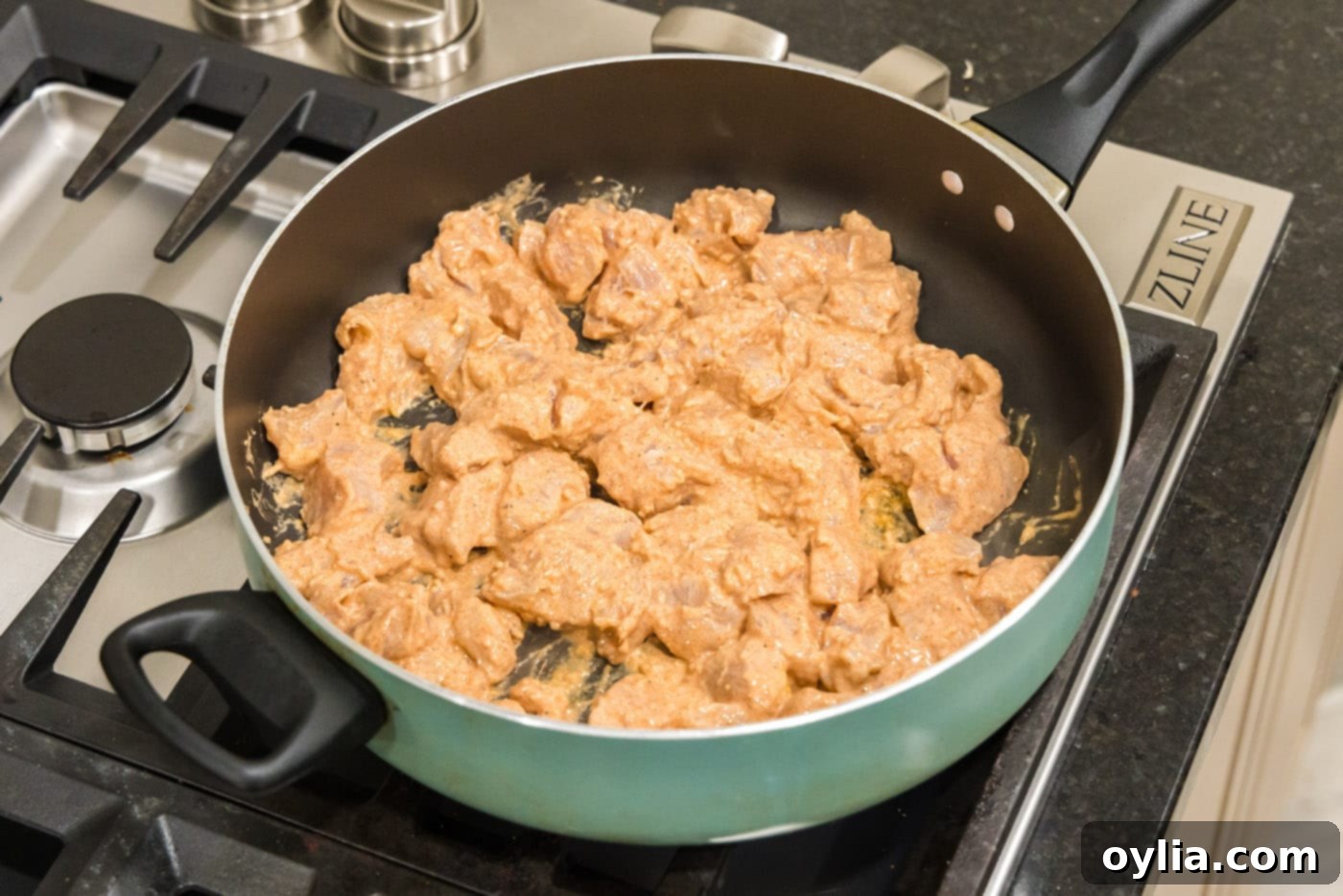 Marinated chicken cubes searing in a heavy-bottomed skillet.