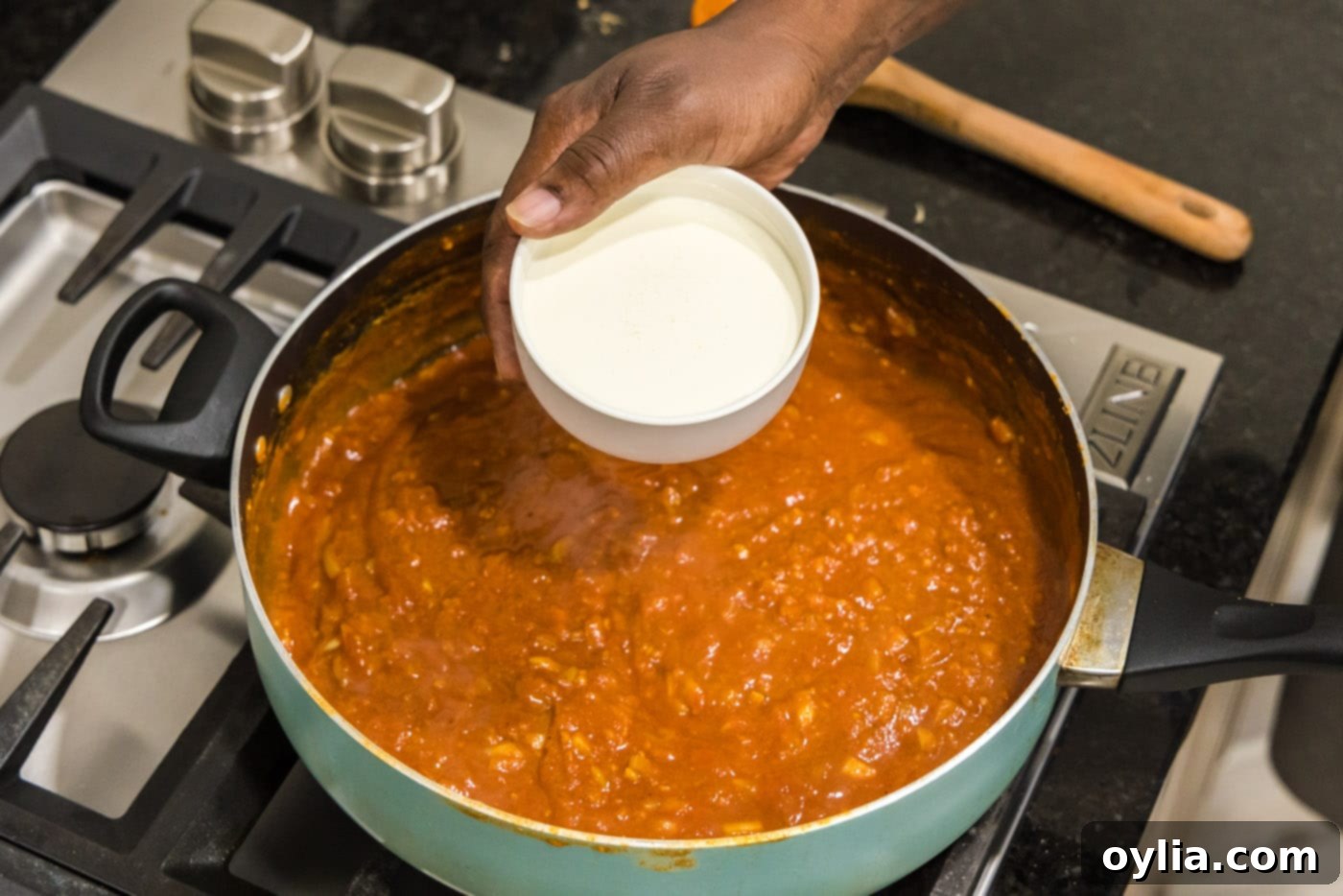 Adding heavy cream to the tomato-based sauce in a skillet for Chicken Tikka Masala.
