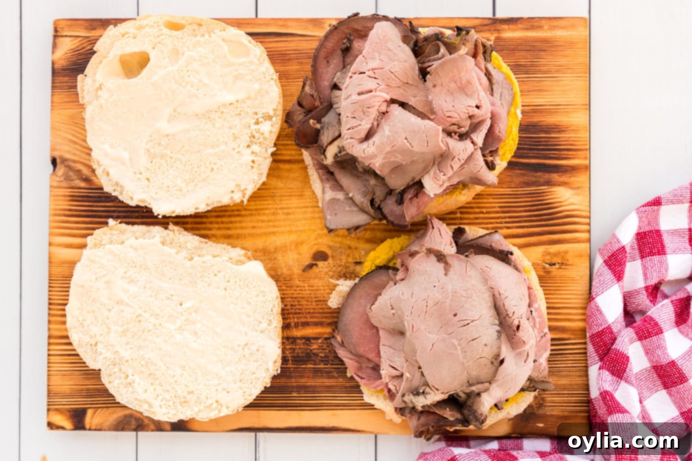 adding roast beef on top of mustard on a bun, creating the first layer