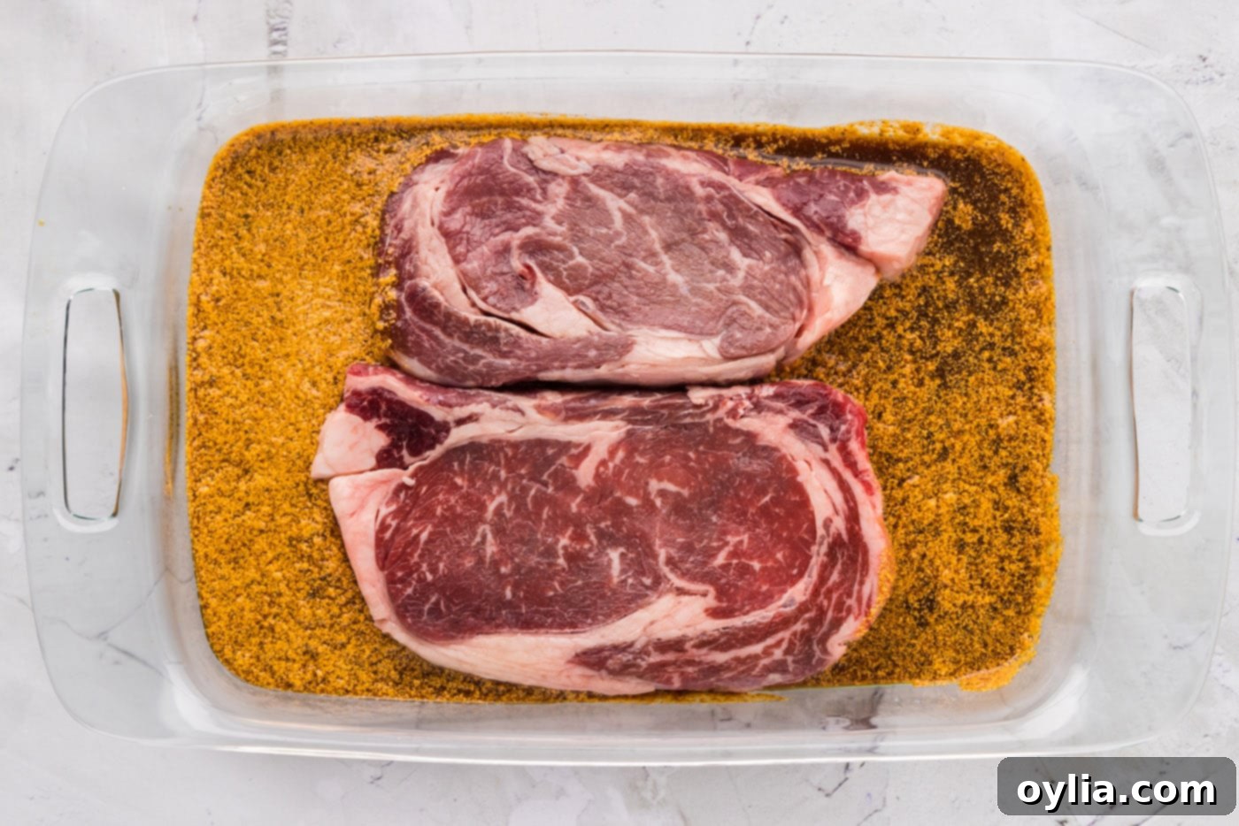 ribeye steak soaking in marinade in a glass dish