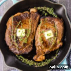 Two Cast Iron Ribeyes in a cast iron pan with butter pats on top