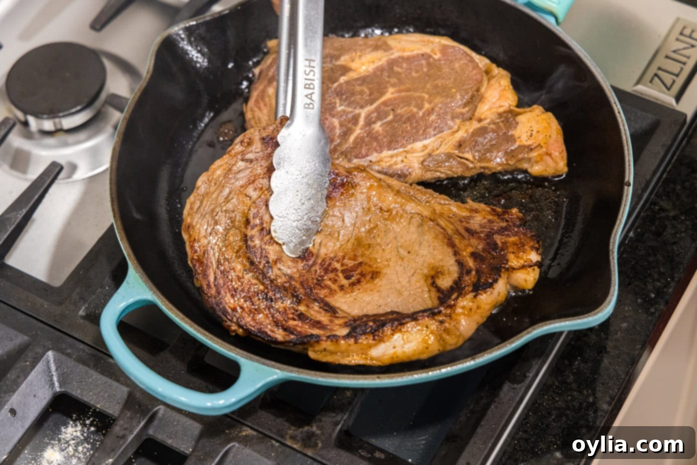 tongs flipping ribeye steak over in a skillet