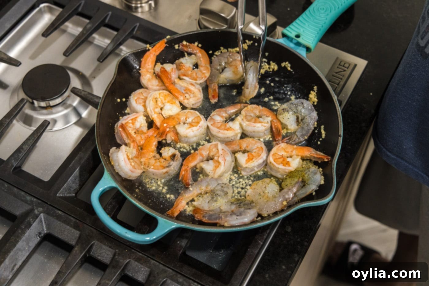 Tongs flipping shrimp over in a skillet to cook evenly and coat in the lemon garlic butter sauce.