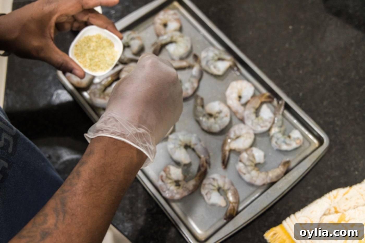 Raw shrimp being seasoned on a baking sheet with garlic salt, preparing for cooking.