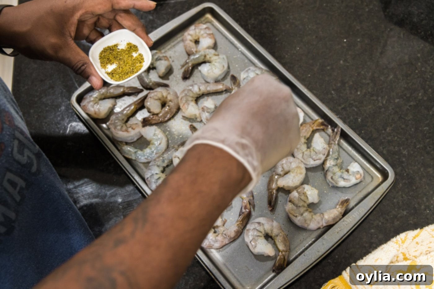 Close-up of shrimp being seasoned with lemon pepper on a baking sheet, ensuring even coverage.