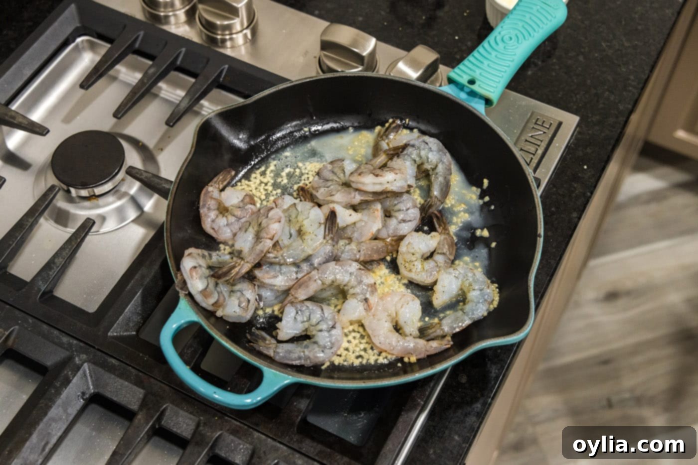 Seasoned raw shrimp cooking in a single layer in a skillet with butter and garlic.