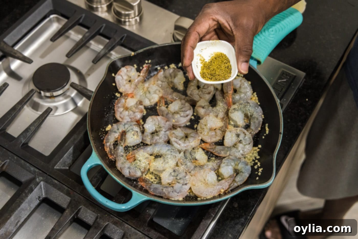 Adding lemon pepper to the shrimp in the skillet, enhancing the citrus and spice.