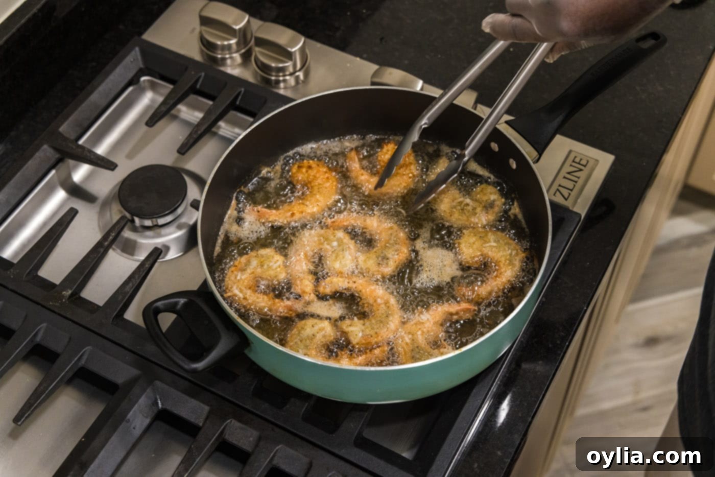tongs flipping coconut shrimp in oil