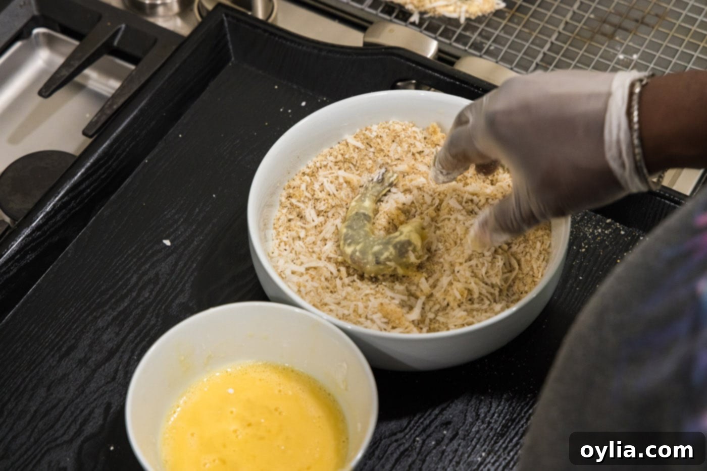 hand dipping dredged shrimp into coconut and panko mixture