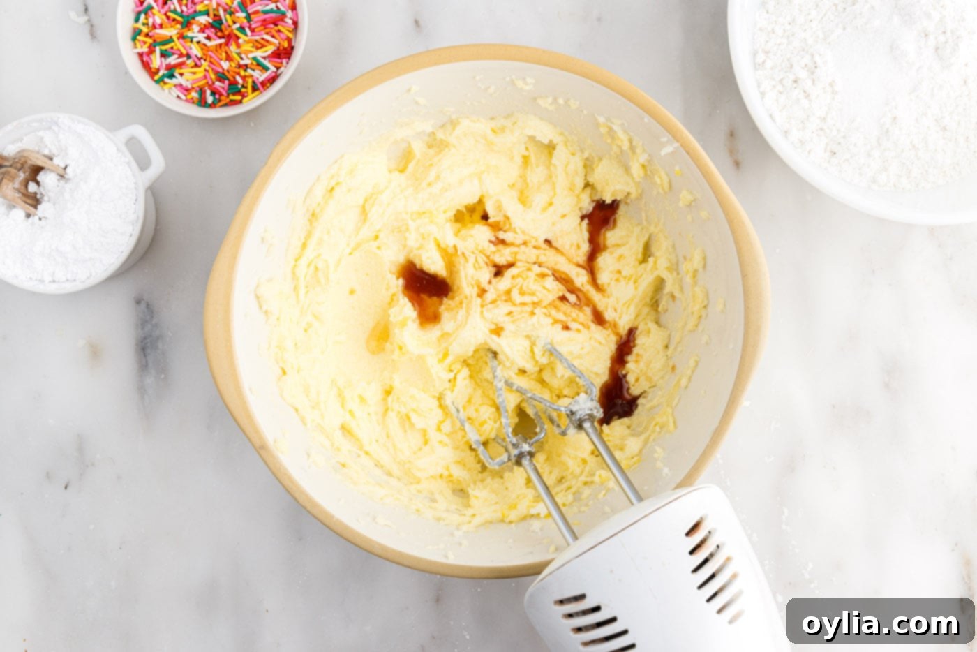 beating vanilla, almond, and oil into butter and sugar mixture in a bowl