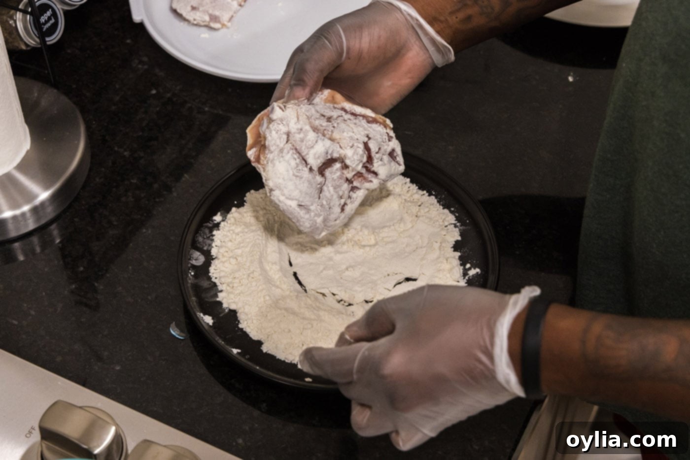 hand dredging chicken thigh in flour
