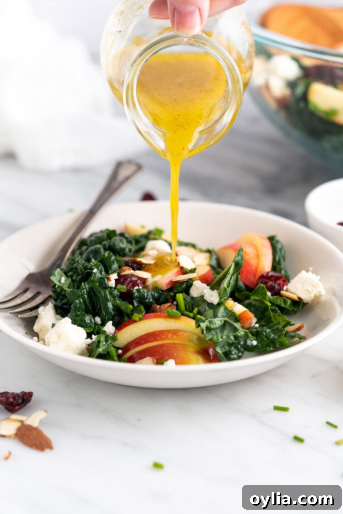 Fresh lemon dressing being drizzled over a bowl of Kale Salad with all ingredients