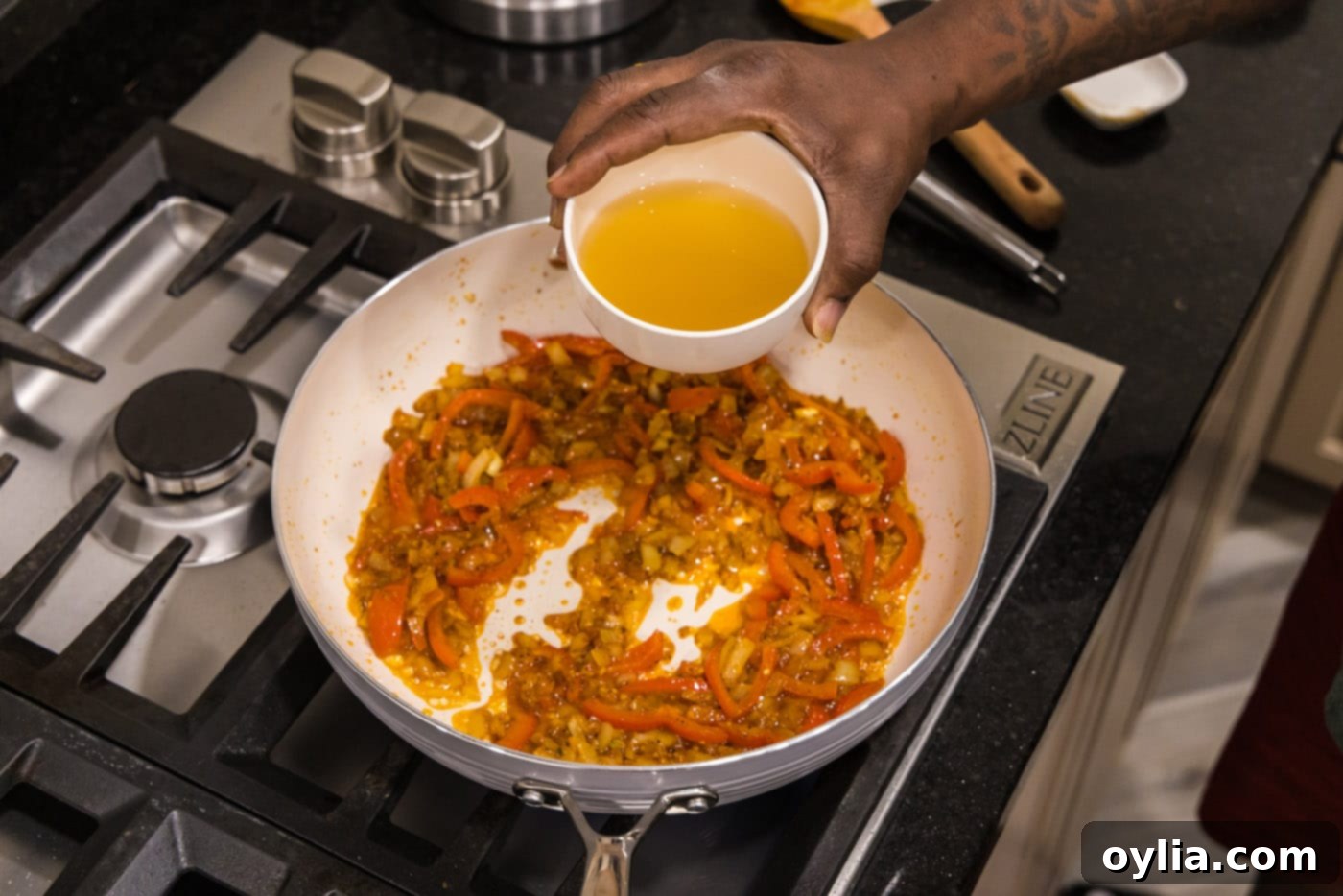 adding chicken stock to curry in a skillet