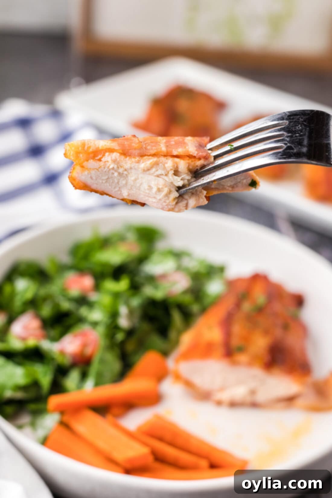 A fork holding a succulent piece of perfectly cooked bacon wrapped chicken, showcasing its crispy exterior and moist interior