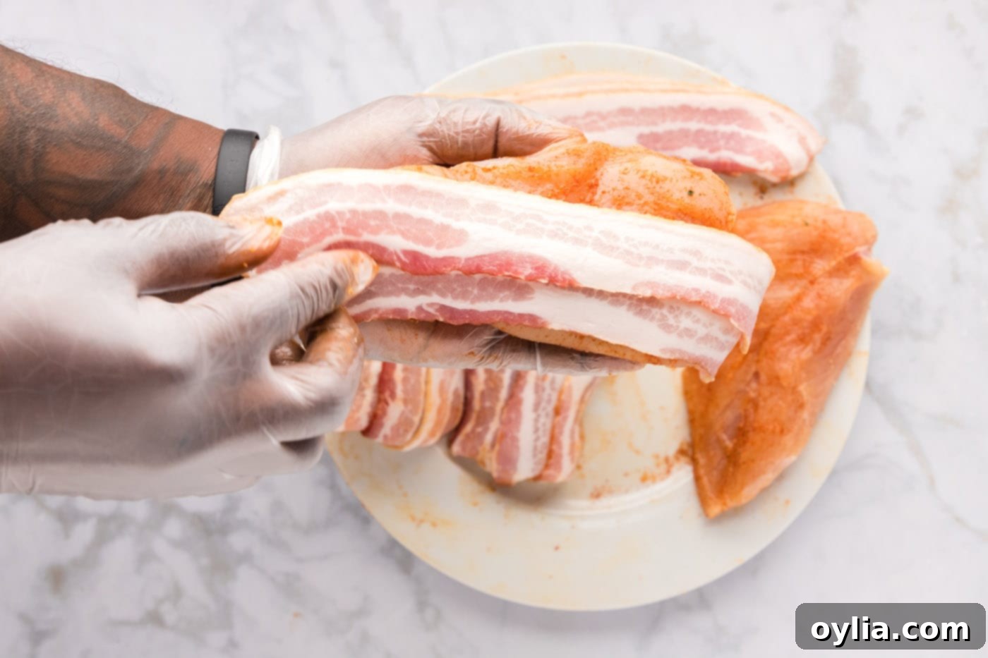 Wrapping raw chicken breasts with strips of center-cut bacon, overlapping each slice for full coverage