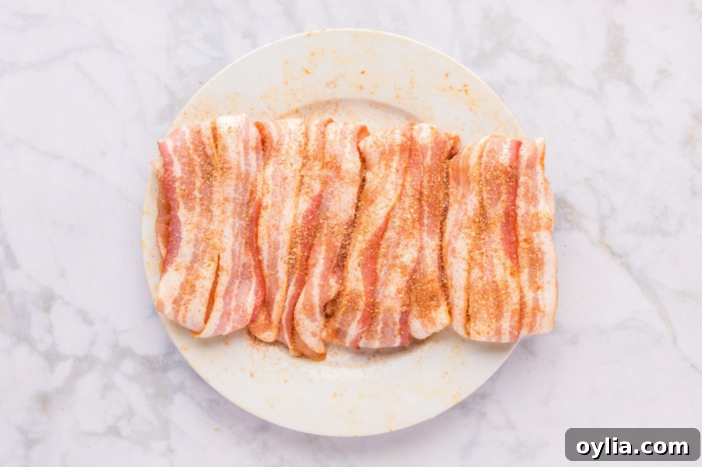 Bacon wrapped chicken breasts on a plate, with a final sprinkle of seasoning on top