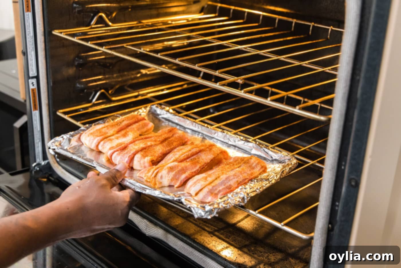 Bacon wrapped chicken baking in the oven on a foil-lined sheet pan, fats rendering