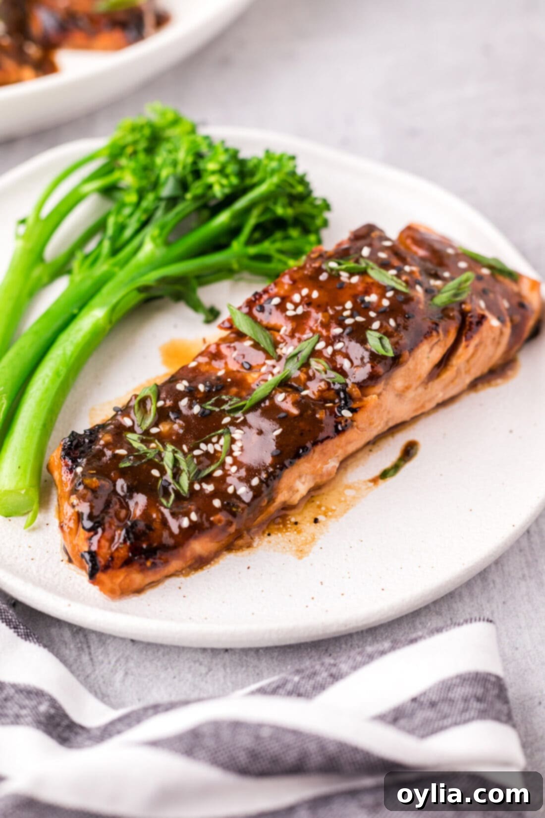 Glazed Teriyaki Salmon 2 Teriyaki Salmon on a plate with broccolini, garnished with sesame seeds and green onions