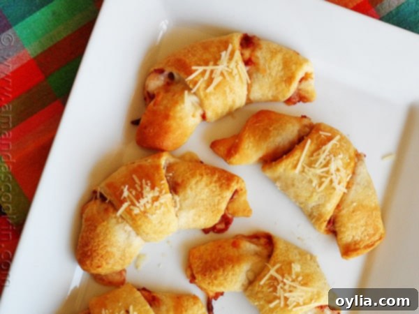 An overhead close up photo of pizza crescent roll ups on a white platter, showcasing the melted cheese and golden crust.