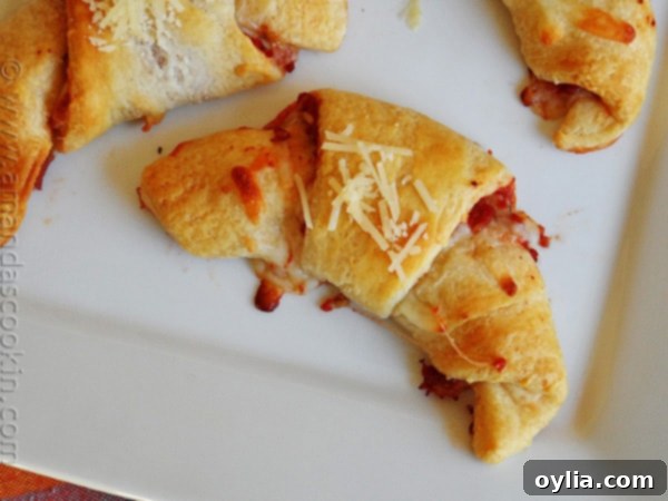 A close up overhead photo of a single pizza crescent roll up on a white platter, showing the crispy exterior.