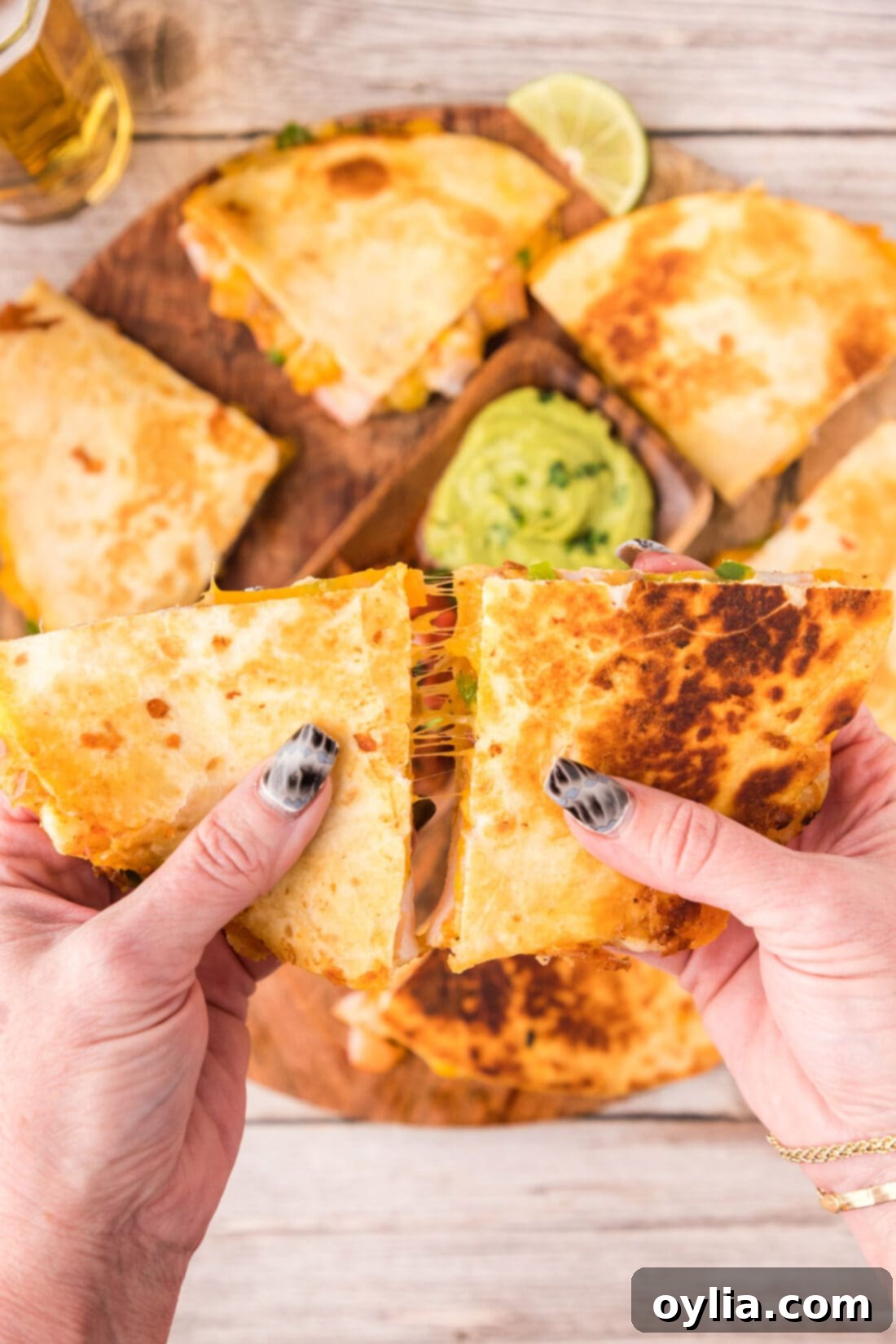 Hands pulling two Shrimp Quesadilla triangles apart, revealing cheesy shrimp and vegetables.