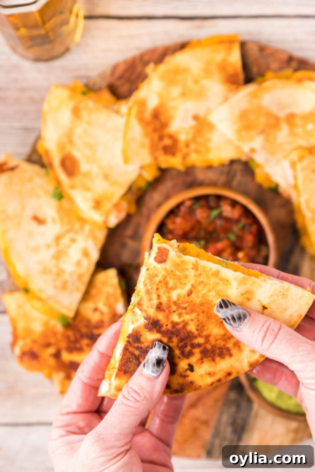Hand holding a triangular slice of Shrimp Quesadilla, showcasing the melted cheese and filling.
