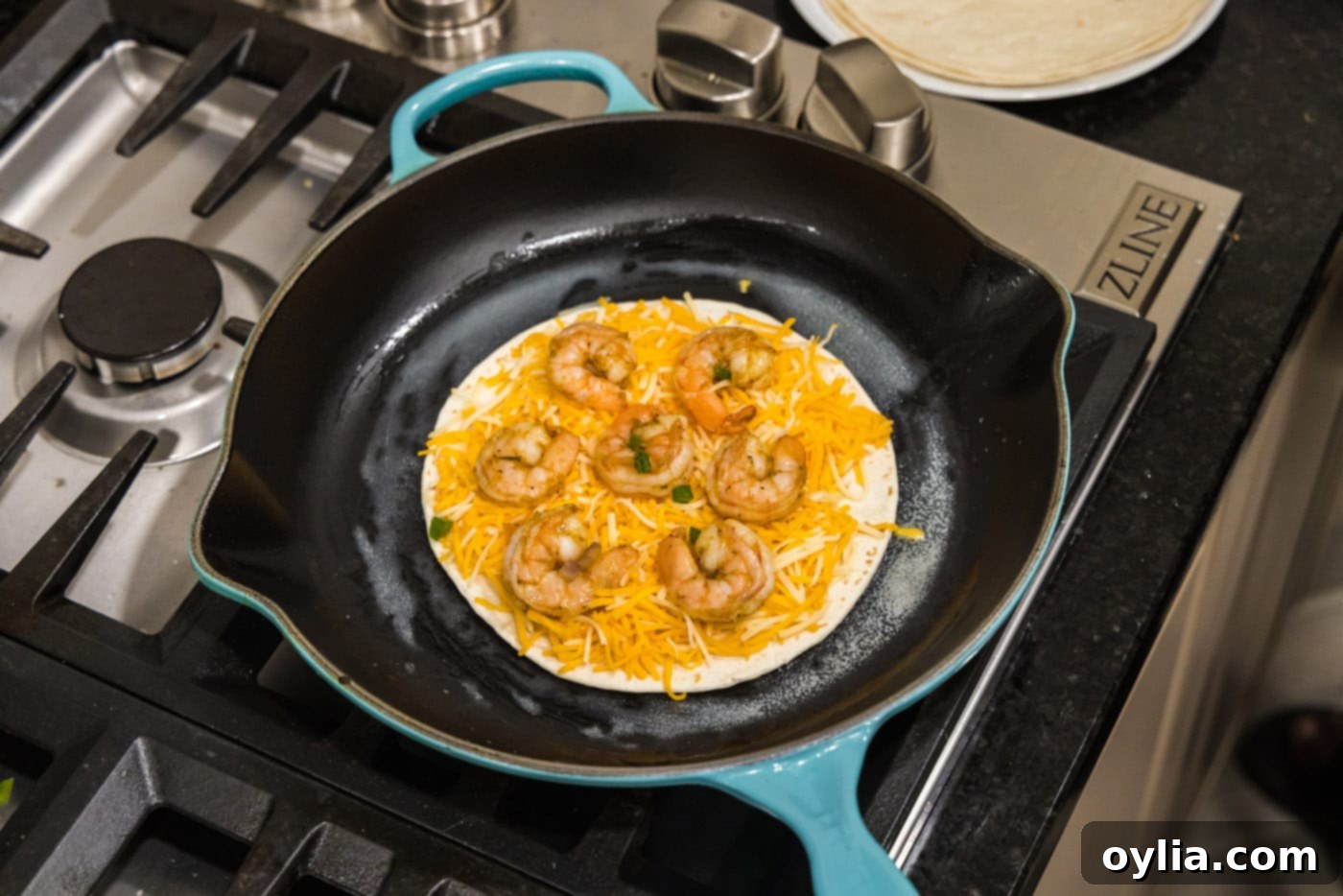 adding seasoned shrimp to tortilla with cheese