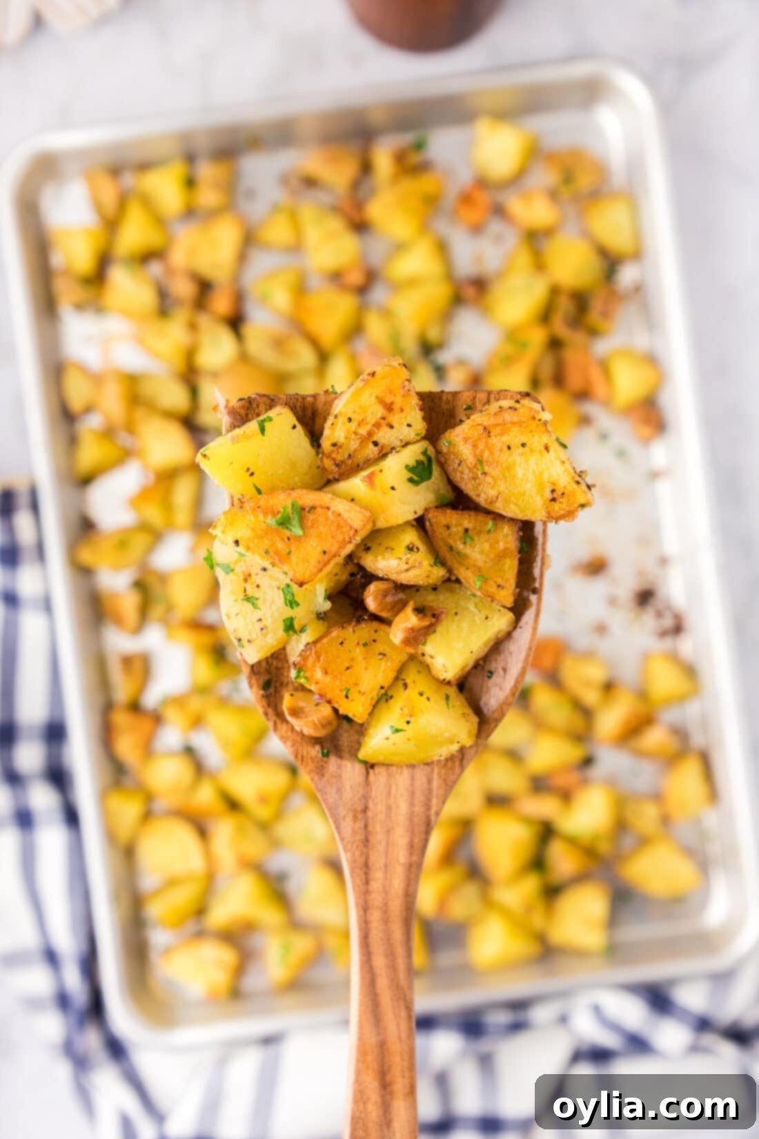 Spatula of Garlic Roasted Potatoes held over a pan of Garlic Roasted Potatoes