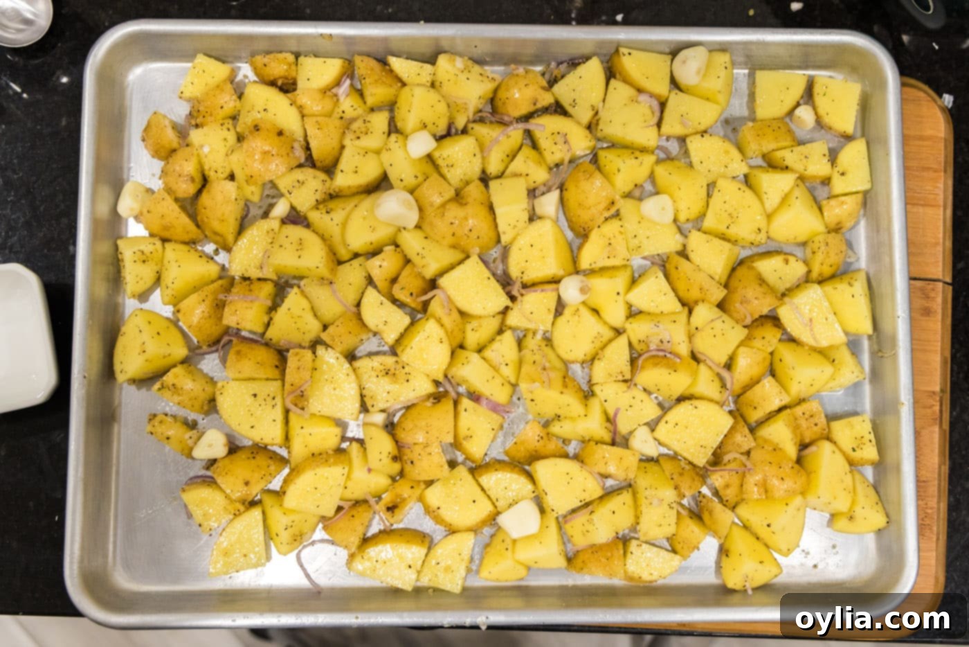 cubed potatoes on a baking sheet with garlic cloves on top