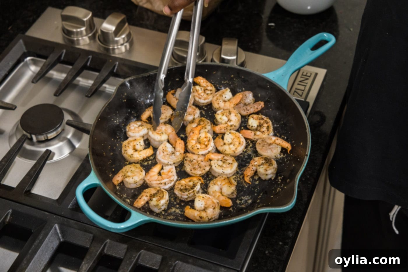 turning shrimp in a skillet with tongs, showing cooked side and uncooked side