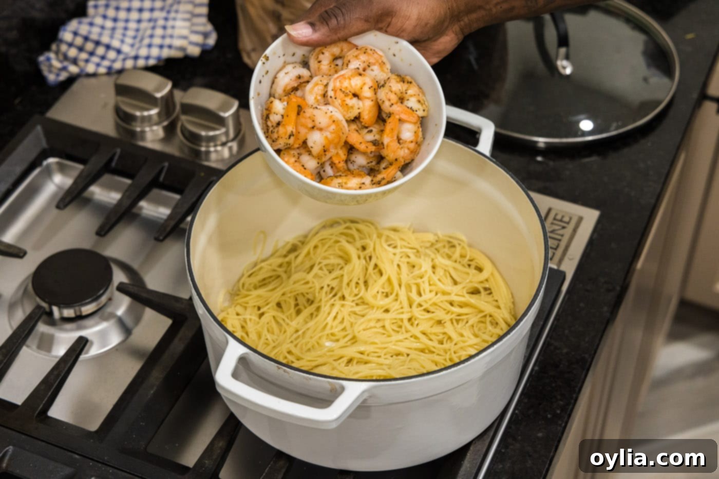 adding shrimp to pasta in a pot with a spatula