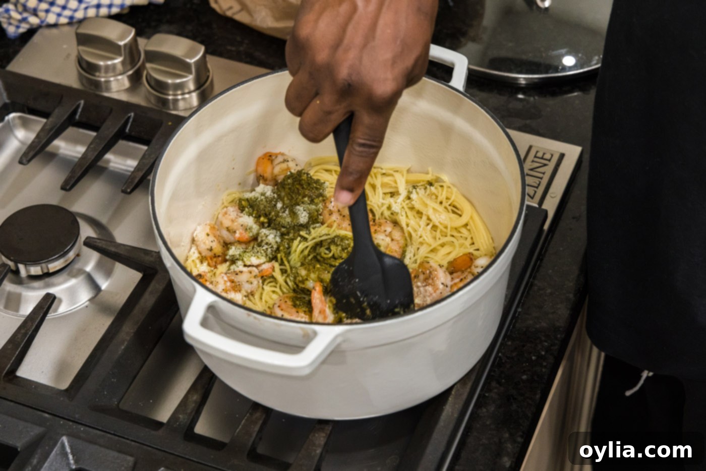 stirring shrimp pesto pasta with a rubber spatula in a pot