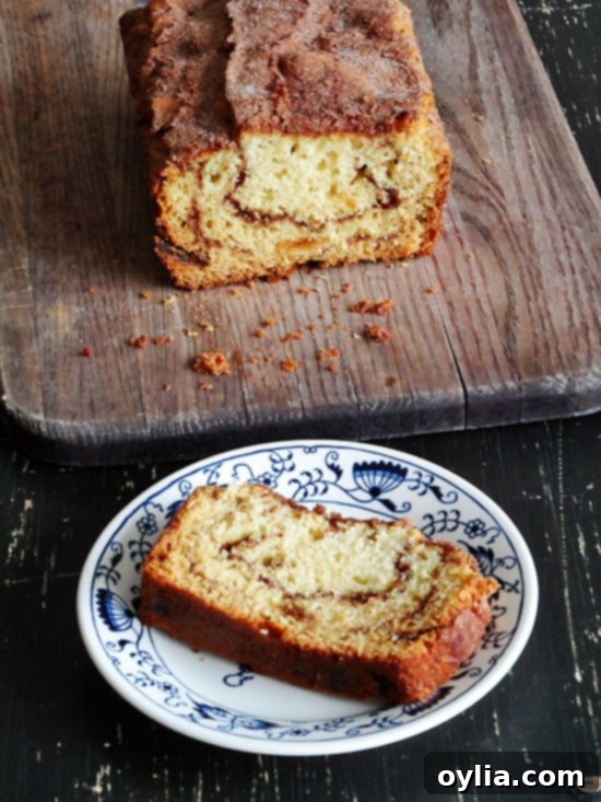 An overhead photo of a loaf of cinnamon raisin swirl quick bread on a wooden cutting board and a slice on a plate, inviting a warm bite.