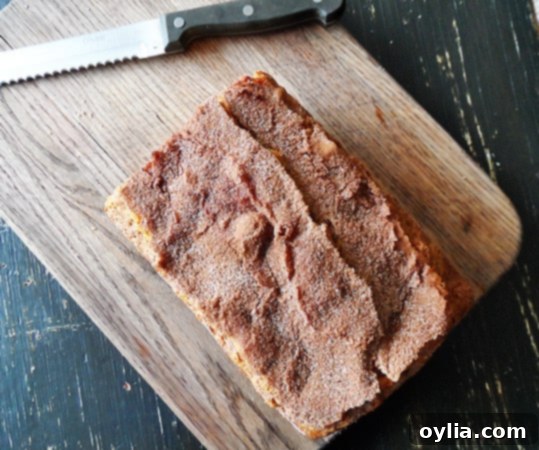 An overhead photo of a freshly baked loaf of cinnamon raisin swirl quick bread on a rustic wooden cutting board, showcasing its golden-brown crust.