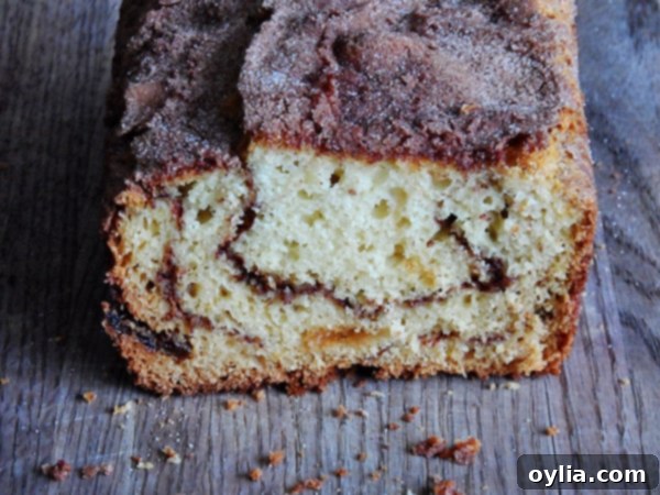 A close up photo of a loaf of cinnamon raisin swirl quick bread cut in half on a wooden cutting board, revealing the intricate cinnamon swirl pattern.