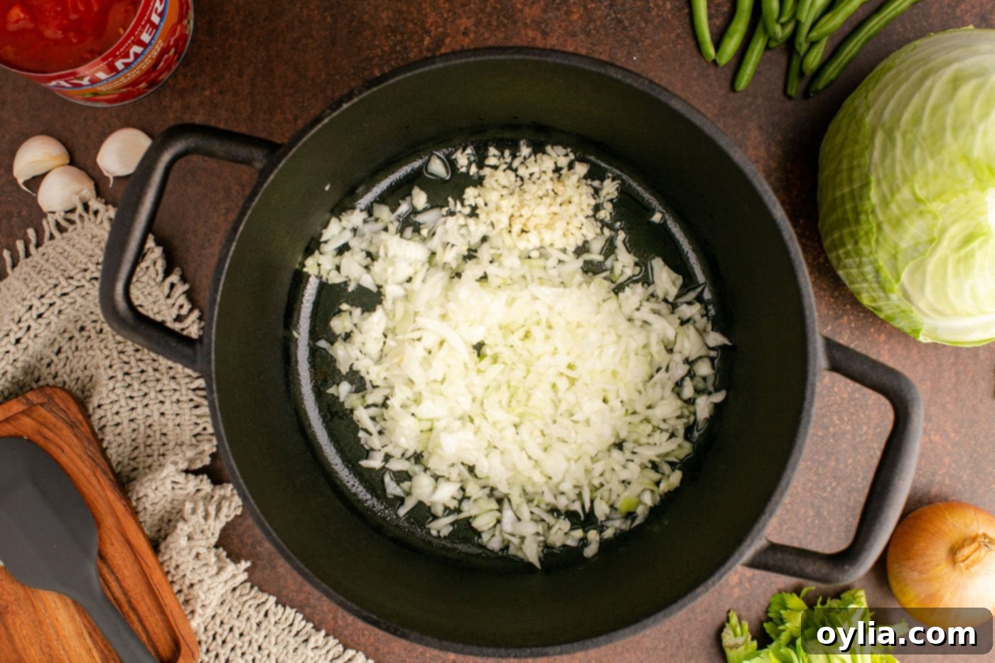Chopped onion and minced garlic sizzling in olive oil within a soup pot, forming the aromatic base of the soup.