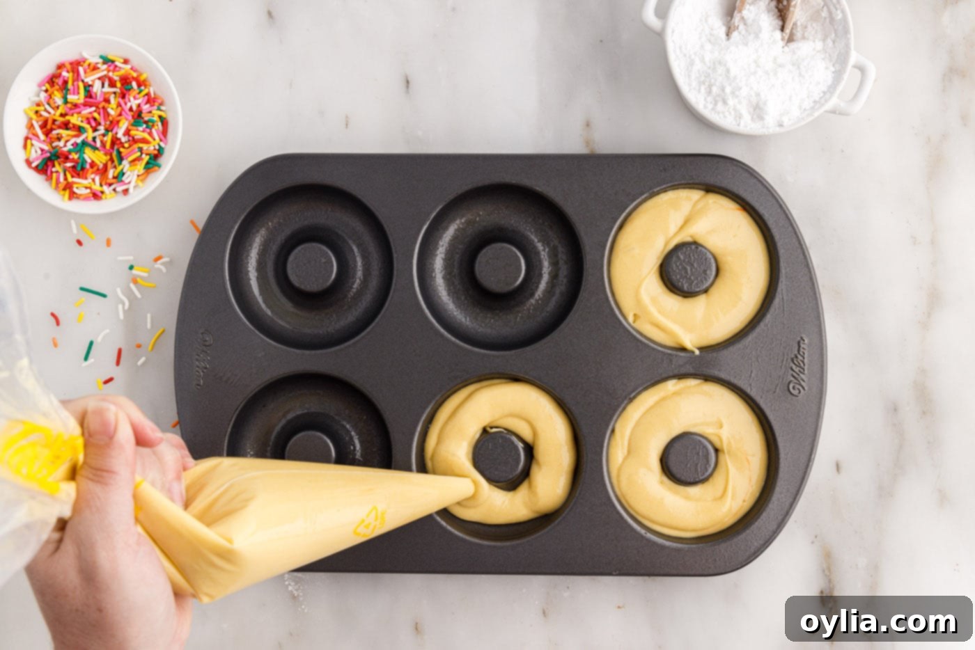 piping cake mix donut batter into a donut pan