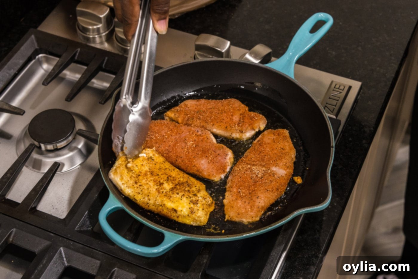 tongs flipping seasoned chicken breasts in a skillet