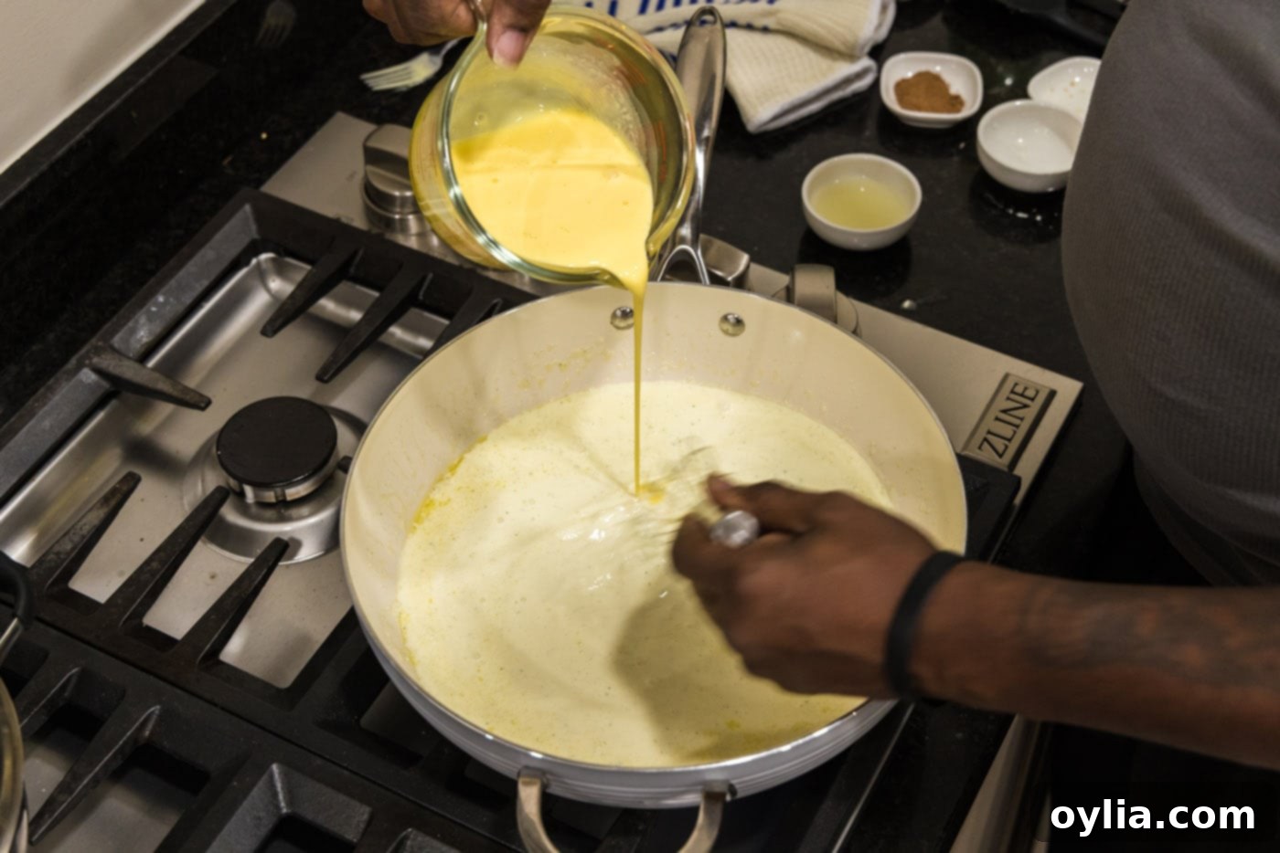 Carefully tempering the egg and cream mixture into the hot sauce in a pan, whisking continuously.