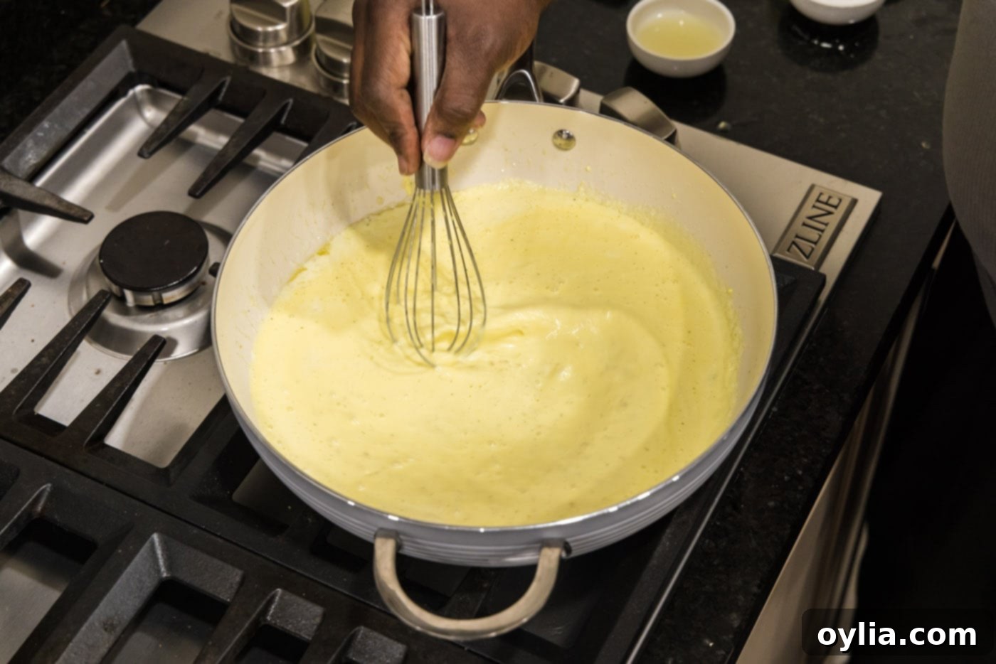 Whisking the tempered egg mixture thoroughly into the creamy sauce in the hot skillet to prevent scrambling.