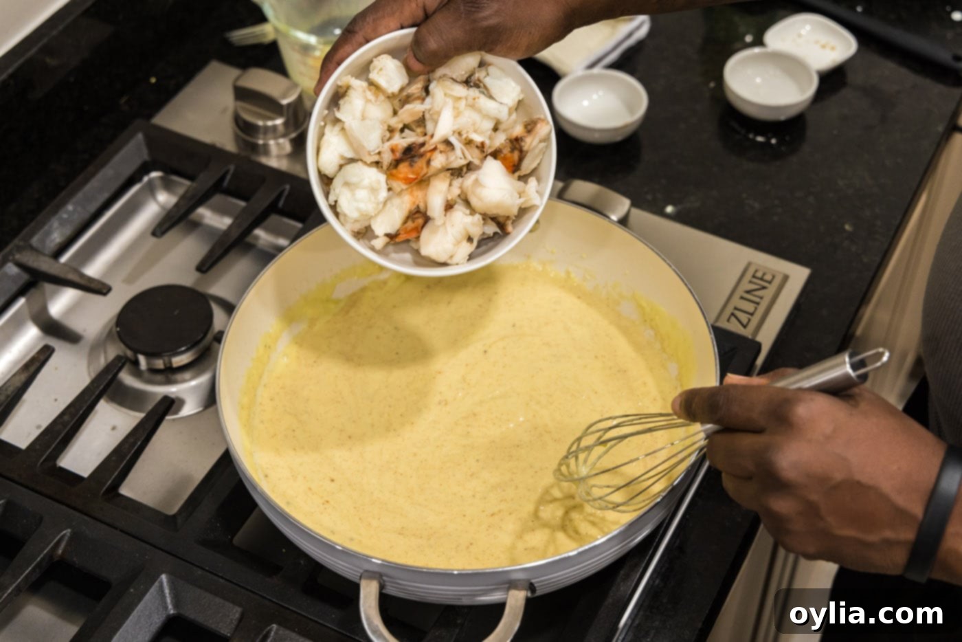 Pouring cooked lobster chunks into the creamy sauce in a skillet, preparing to combine the ingredients.