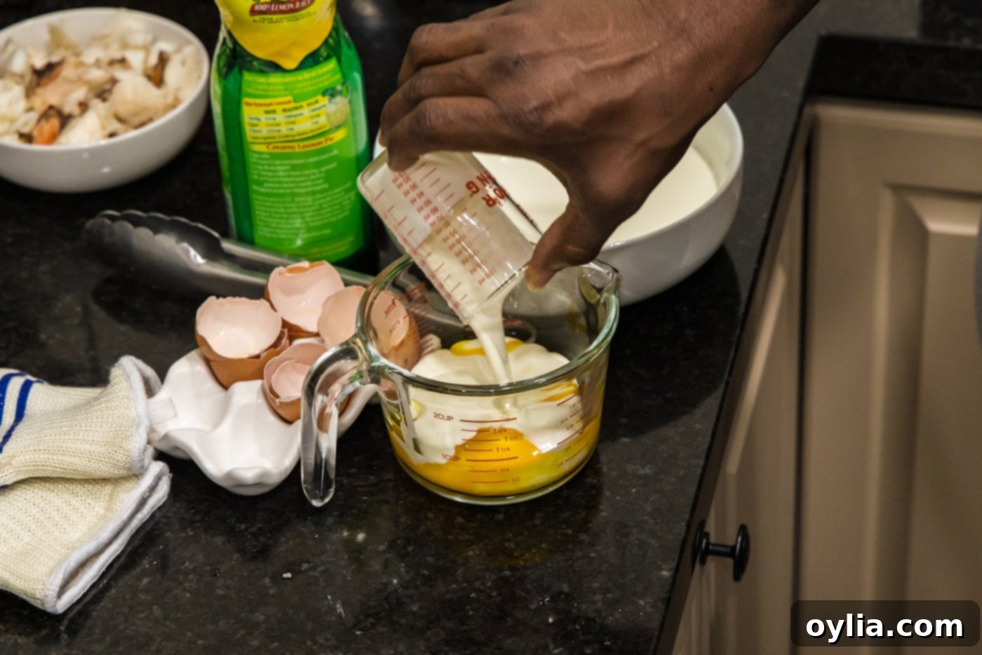 Pouring heavy cream into egg yolks in a measuring cup, preparing the tempering mixture for Lobster Newburg.