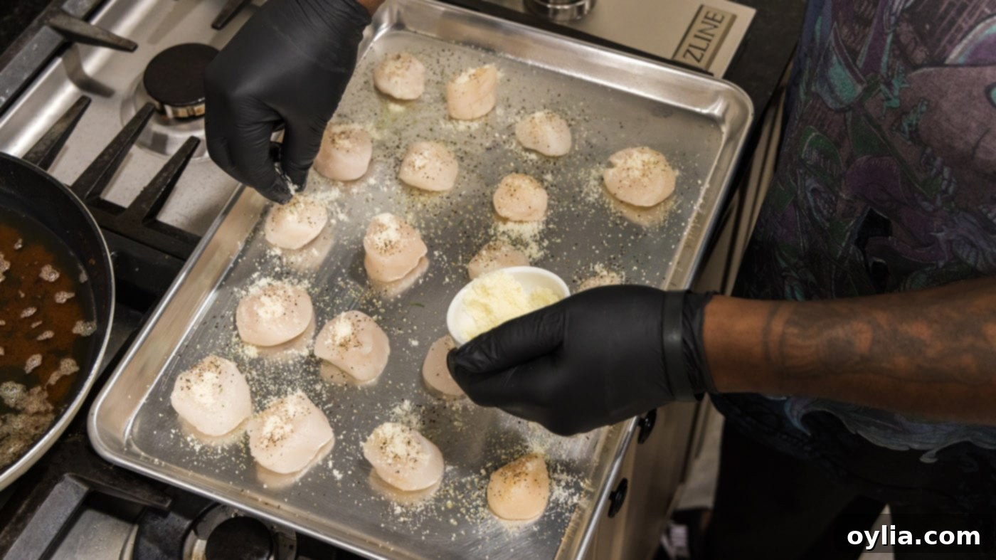 A hand sprinkling grated Parmesan cheese over scallops with breadcrumbs