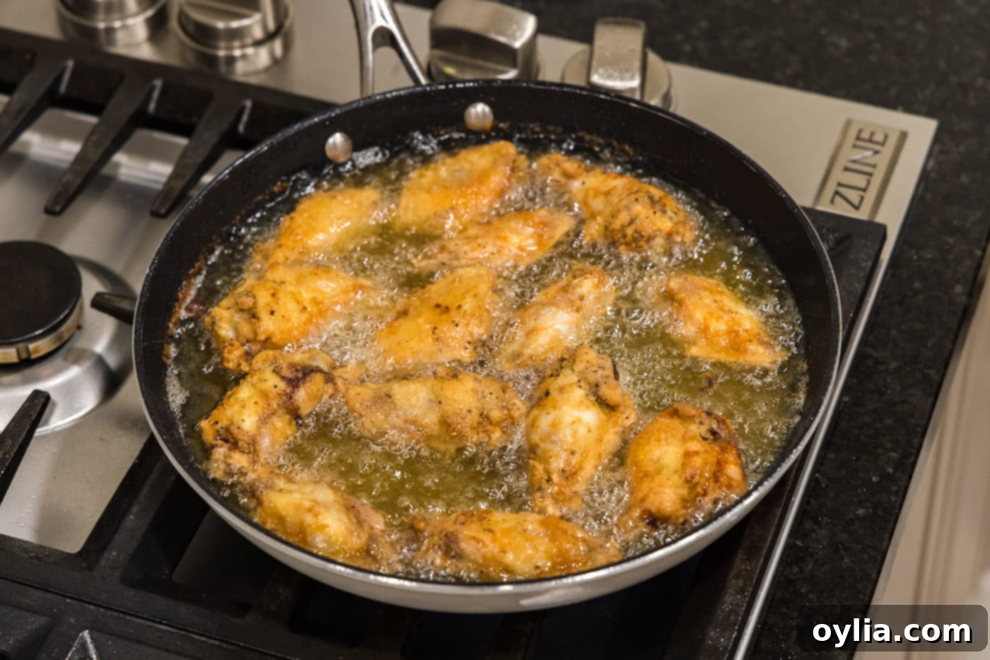 A skillet full of golden-brown fried chicken wings, perfectly cooked and crispy, submerged in hot oil.
