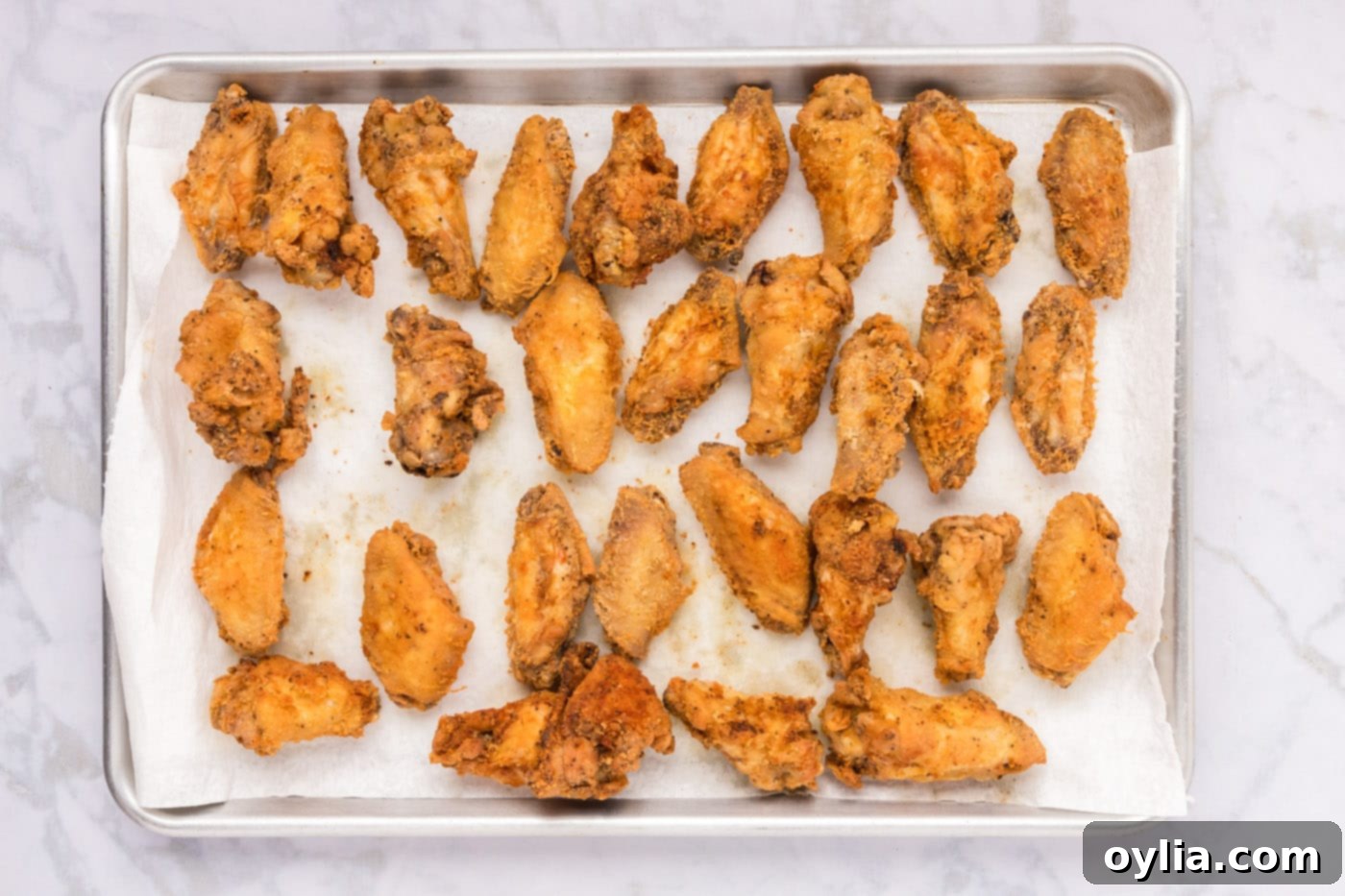 Freshly fried chicken wings resting on a wire rack lined with paper towels on a baking sheet, allowing excess oil to drain.